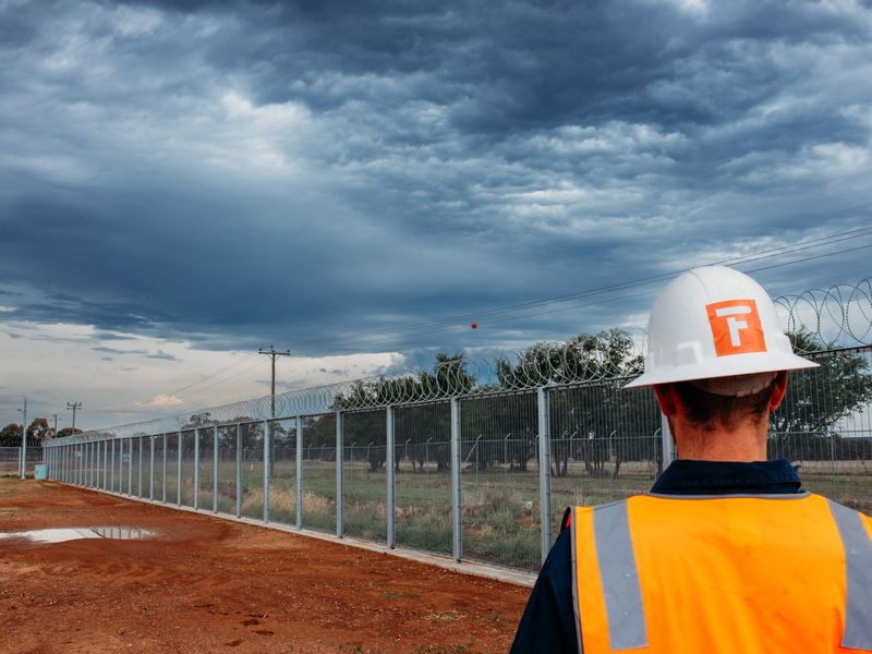 Fencepac crew member overlooking security fencing installation with branded hard hat and hi-vis